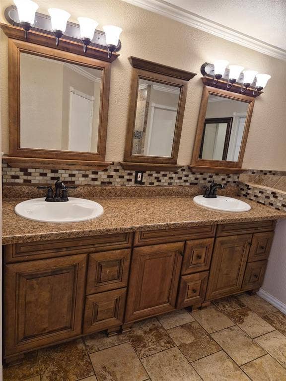 1088 Magnolia Lane, Cedar Hill, TX 75104 Dual-sink vanity featuring stained wood cabinetry, stone-finish countertops, mosaic tile backsplash, and matching wood-framed wall mirrors with multi-bulb light fixtures