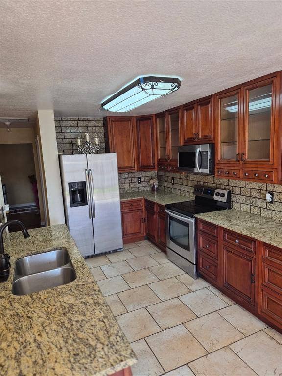 1088 Magnolia Lane, Cedar Hill, TX 75104 Kitchen featuring wood cabinetry with glass-panel upper doors, stone-finish countertops, tile backsplash, stainless steel appliances, and tile flooring