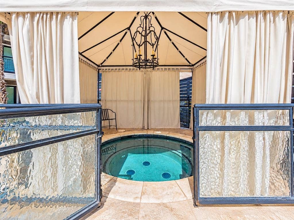 7730 Meadow Park Drive, #222, Dallas, TX 75230 Outdoor spa featuring a circular in-ground basin, stone-tile surround, metal-frame gazebo, and wrought-iron chandelier