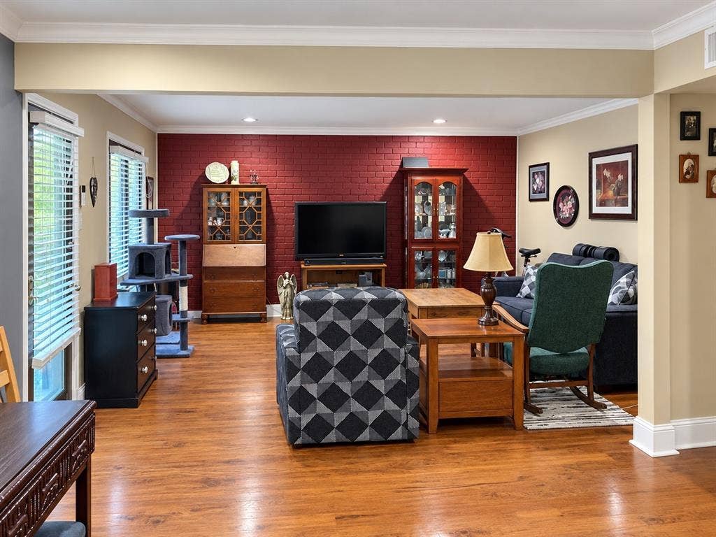7730 Meadow Park Drive, #222, Dallas, TX 75230 Living area featuring a red painted brick accent wall, wood-finish flooring, recessed lighting, and crown molding