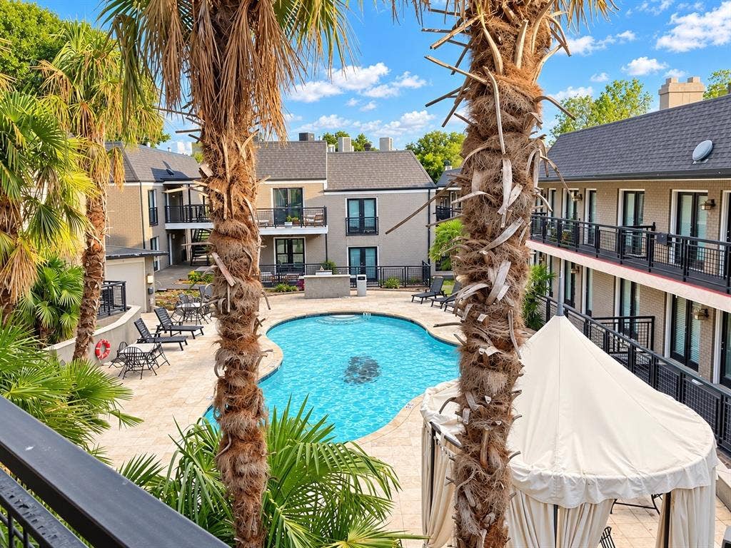 7730 Meadow Park Drive, #222, Dallas, TX 75230 Swimming pool with surrounding stone-finished patio, mature palm trees, and multi-story buildings featuring exterior metal railings