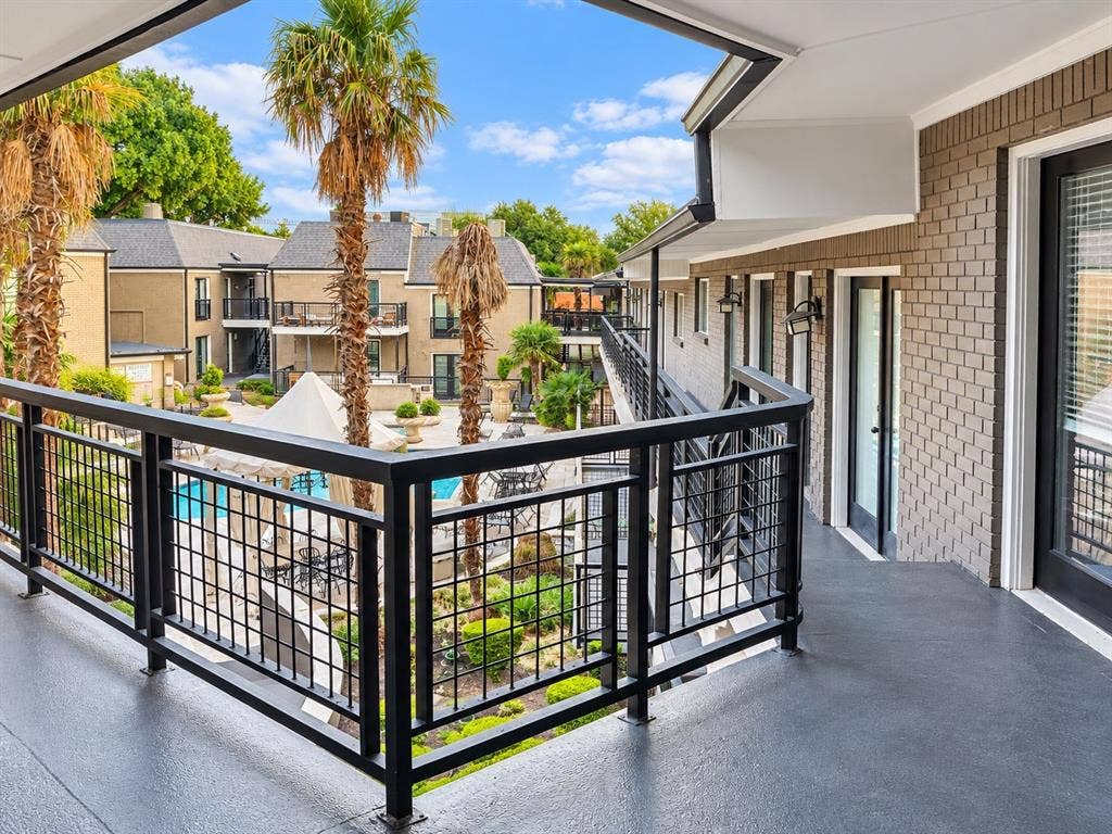 7730 Meadow Park Drive, #222, Dallas, TX 75230 Covered balcony featuring black metal railings, textured concrete flooring, painted brick exterior, and wall-mounted exterior lighting