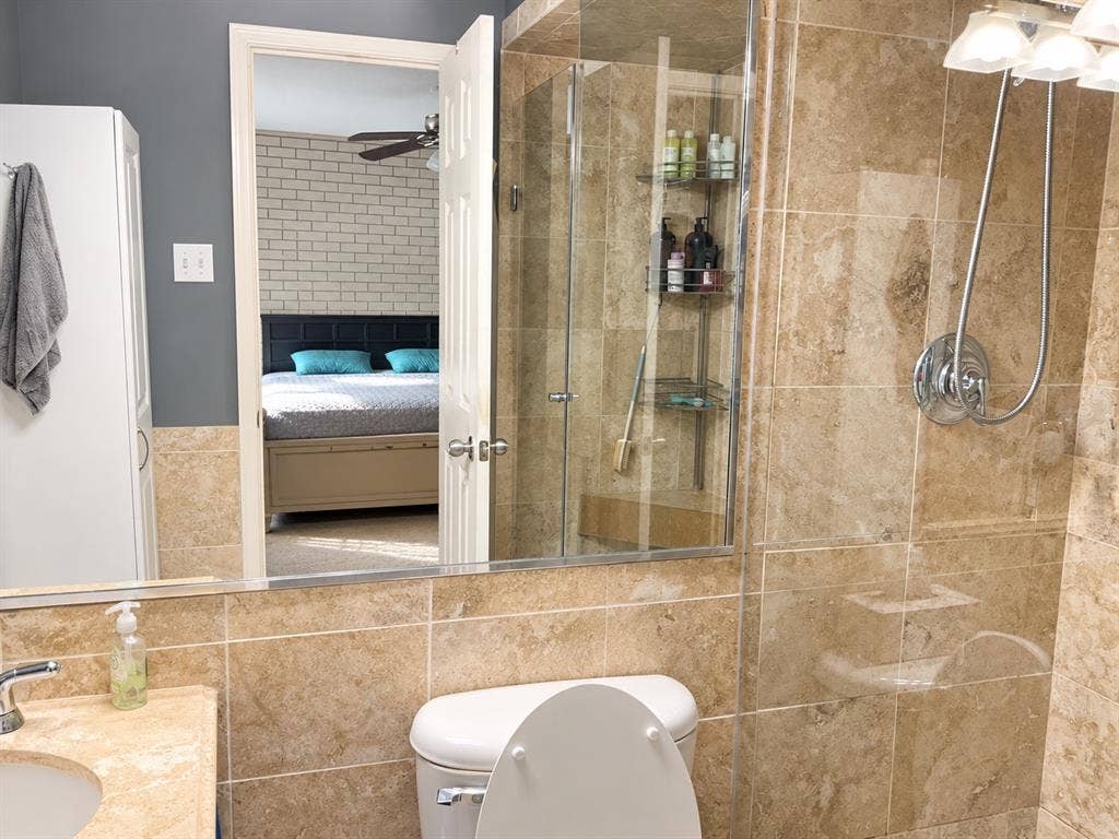 7730 Meadow Park Drive, #222, Dallas, TX 75230 Walk-in shower with stone-tile surround, glass enclosure, and multi-setting showerhead, paired with a matching stone-tile backsplash and vanity countertop