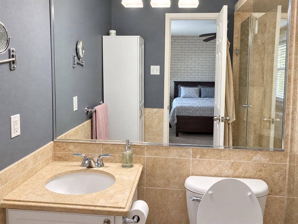 7730 Meadow Park Drive, #222, Dallas, TX 75230 Bathroom featuring a neutral stone-finish countertop, undermount sink, glass-enclosed shower, built-in storage cabinet, and large-scale vanity mirror