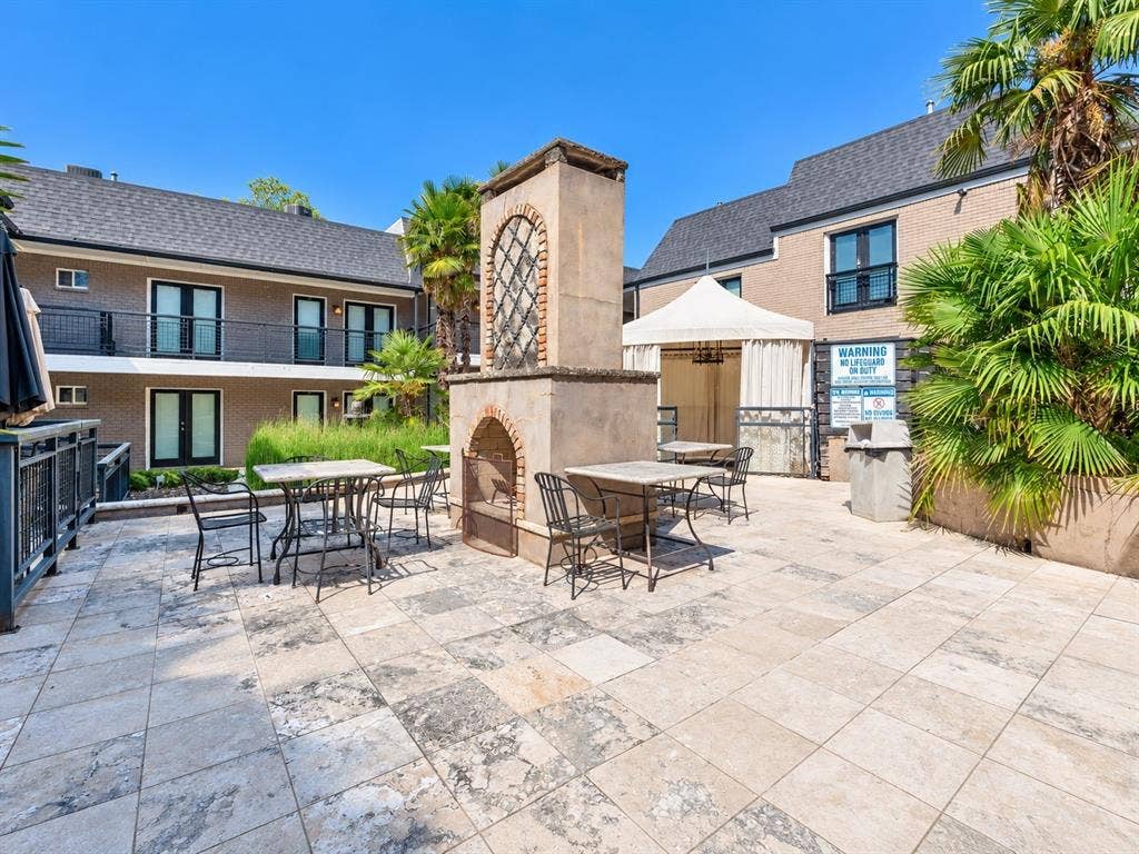 7730 Meadow Park Drive, #222, Dallas, TX 75230 Outdoor patio featuring a stone-clad central fireplace, tile flooring, and integrated wrought-iron railings