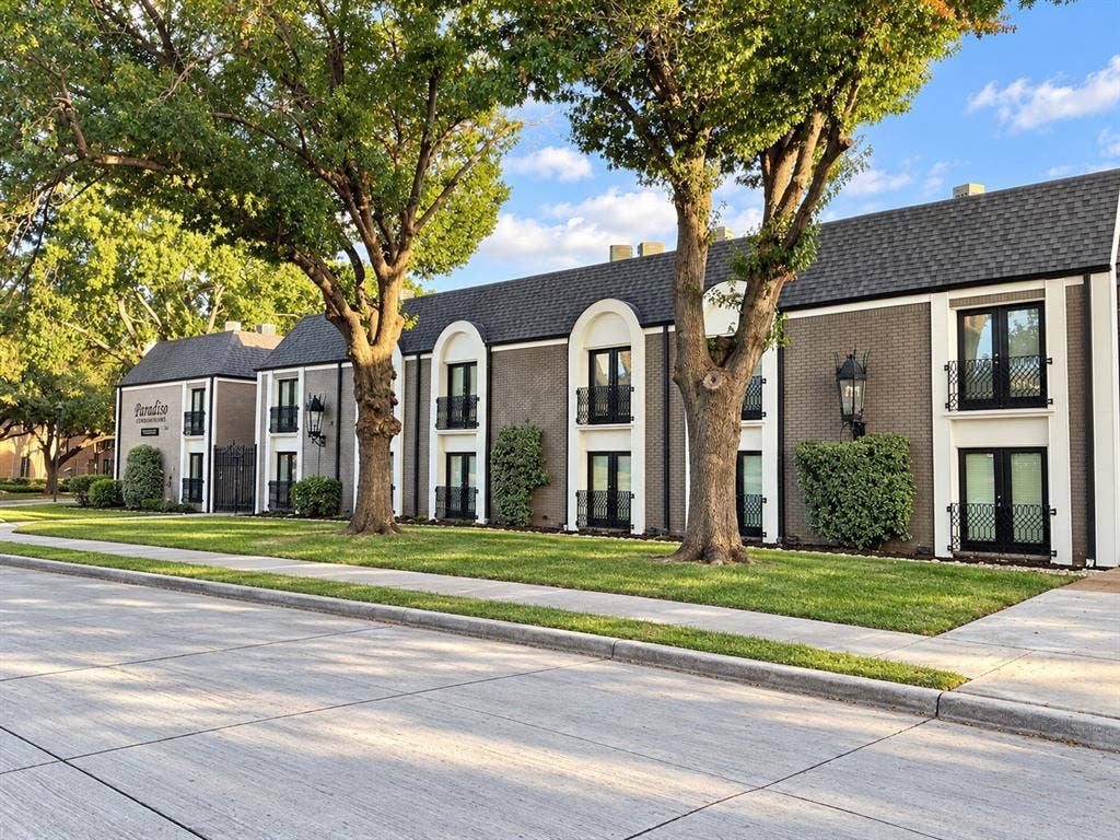 7730 Meadow Park Drive, #222, Dallas, TX 75230 Two-story exterior featuring dark brick masonry with white arched trim, black metal balcony railings, multi-light glass doors, and dark shingled roofing