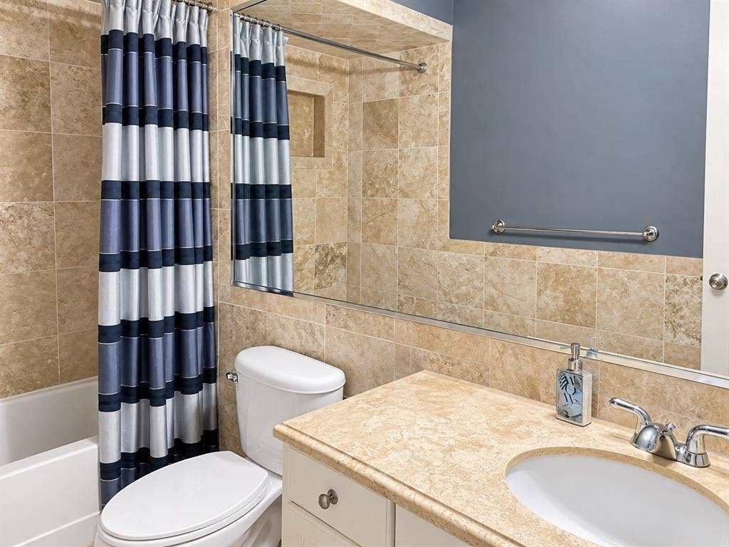 7730 Meadow Park Drive, #222, Dallas, TX 75230 Bathroom featuring floor-to-ceiling stone-tiled walls, a built-in recessed wall niche, a large plate glass mirror, and a vanity with a solid surface countertop and integrated oval sink