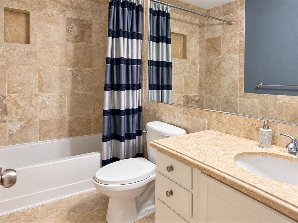 7730 Meadow Park Drive, #222, Dallas, TX 75230 Bathroom featuring full-height wall tiling, built-in recessed shower shelving, a vanity with a stone-finish countertop, an oval under-mount sink, and a full-width wall mirror