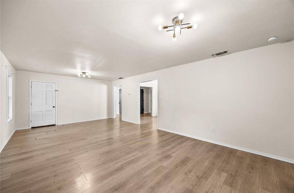 Neutral-toned interior space featuring wood-finish flooring, multi-directional ceiling light fixtures, and a six-panel door
