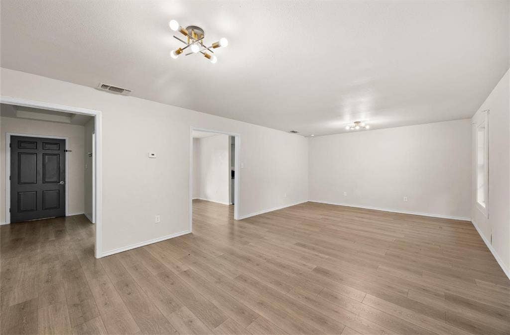 Open-concept interior featuring light-toned wood-finish flooring, neutral walls, and contemporary multi-arm brass finish light fixtures