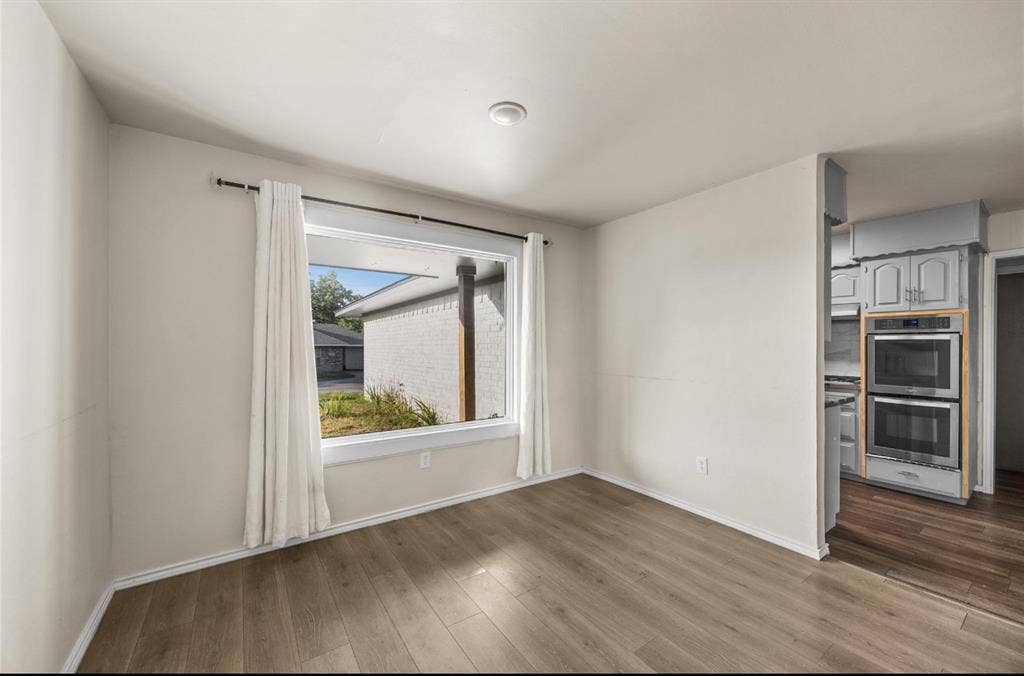 Room featuring wood-finish flooring, a large picture window, and recessed lighting, with a built-in stainless steel double oven in the kitchen