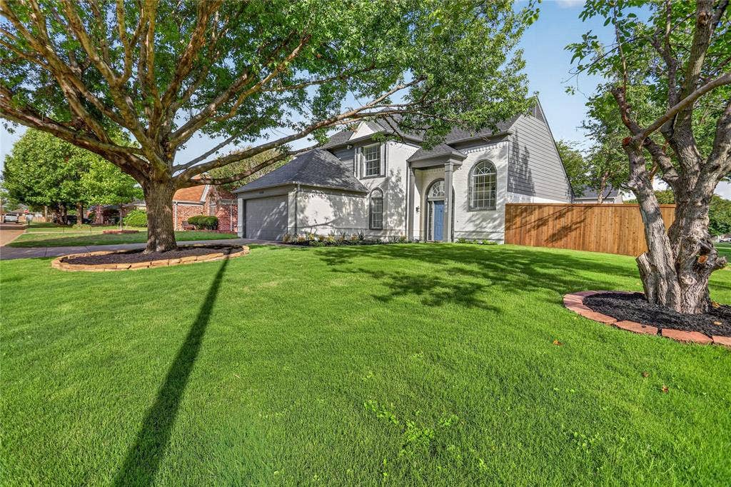 Two-story exterior featuring a brick and composite siding facade, arched entryway, multi-paned windows, an attached two-car garage, and landscaped lawn with mature trees
