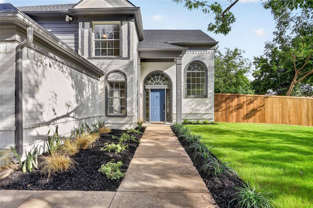 Painted brick exterior featuring arched windows, a multi-pane front door with a transom, concrete walkway, and landscaped garden beds