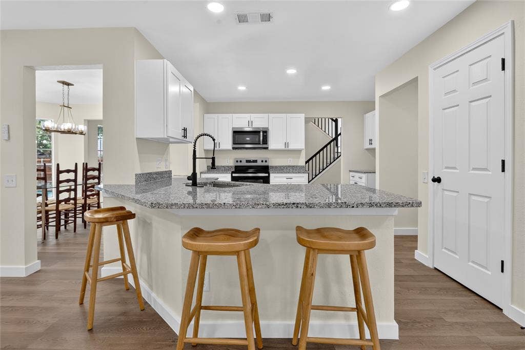 Kitchen featuring white shaker-style cabinetry, speckled stone countertops, a stainless steel microwave and range, a high-arc matte black faucet, and wood-finish flooring