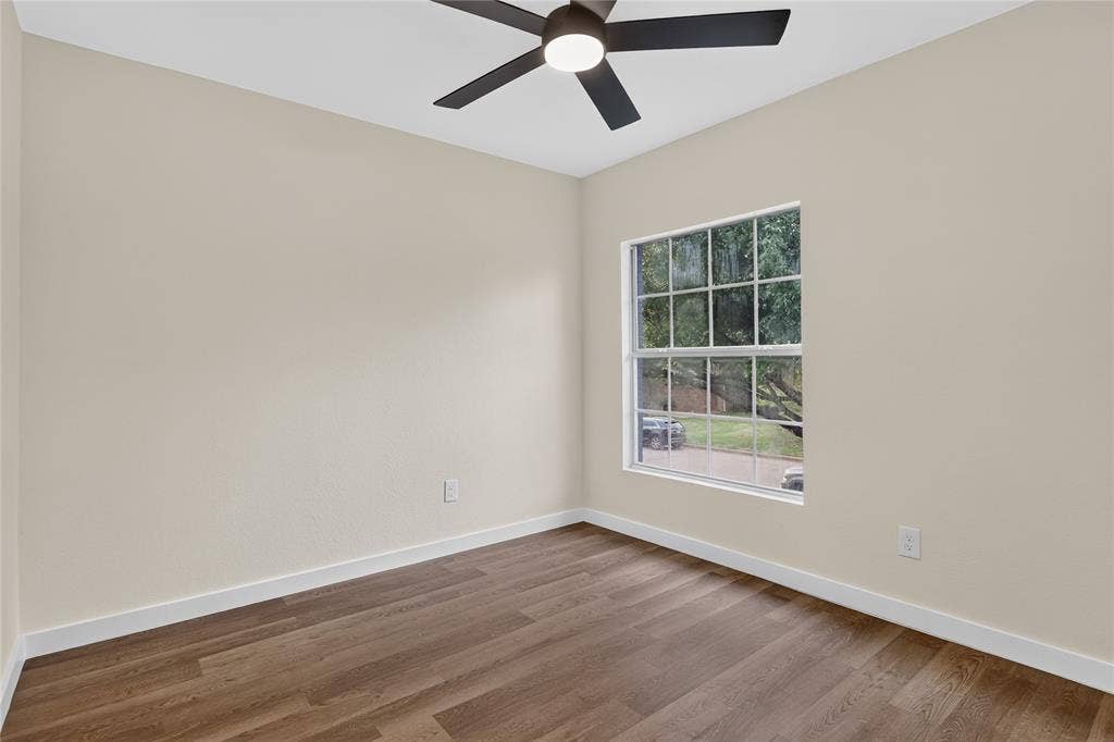 Room featuring neutral wall paint, wood-finish flooring, multi-pane window, and a matte black ceiling fan with integrated lighting