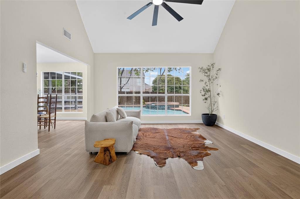 Vaulted ceilings featuring a central matte black ceiling fan, wood-finish flooring, and large multi-pane windows showcasing an in-ground swimming pool and spa
