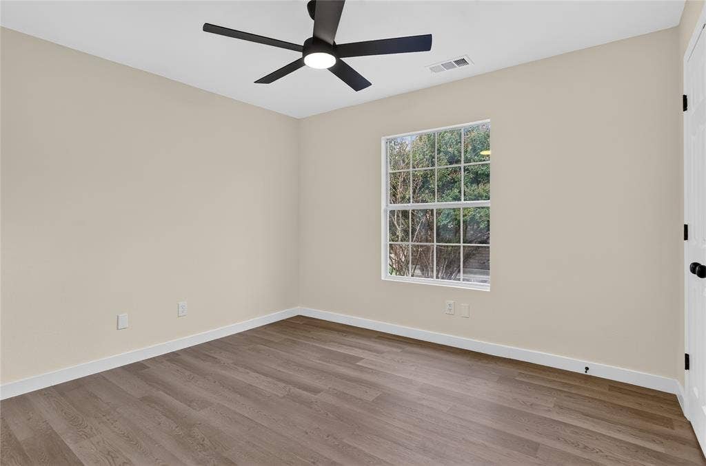 Neutral wall tones, wood-finish flooring, multi-pane window, and matte black ceiling fan with integrated lighting