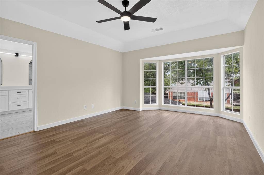 Tray ceiling with a matte black modern ceiling fan, wood-finish flooring, and a multi-pane bay window