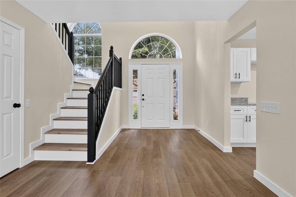 Foyer featuring high ceilings, wood-finish flooring, a staircase with a black handrail and balusters, and an arched entryway door with sidelights