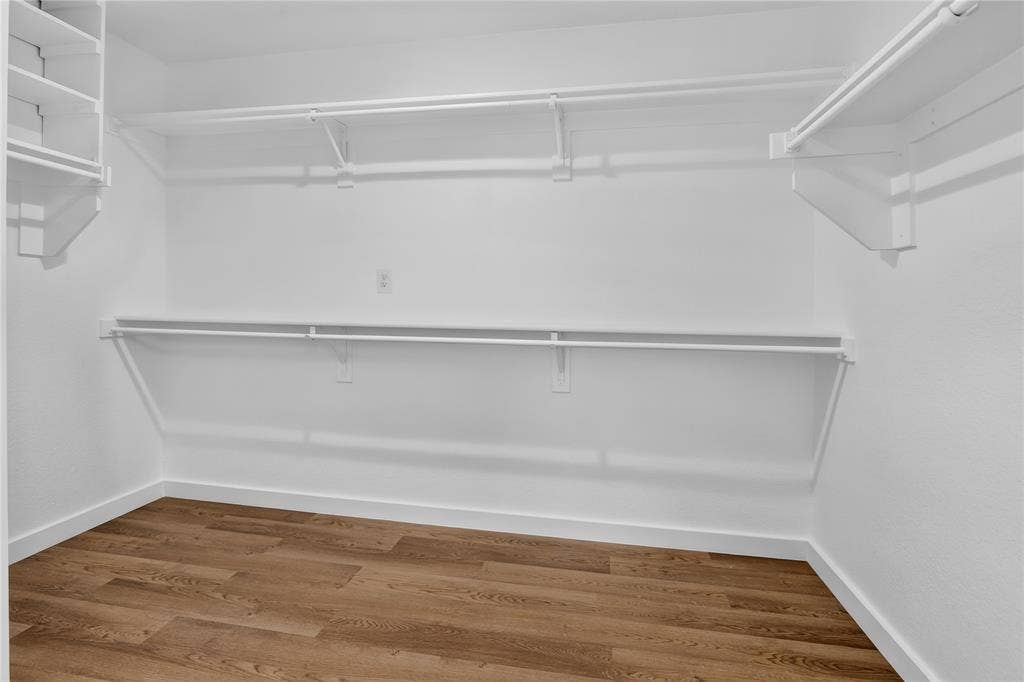 Walk-in storage area featuring wood-finish flooring, white walls, and multi-level built-in shelving with integrated rods