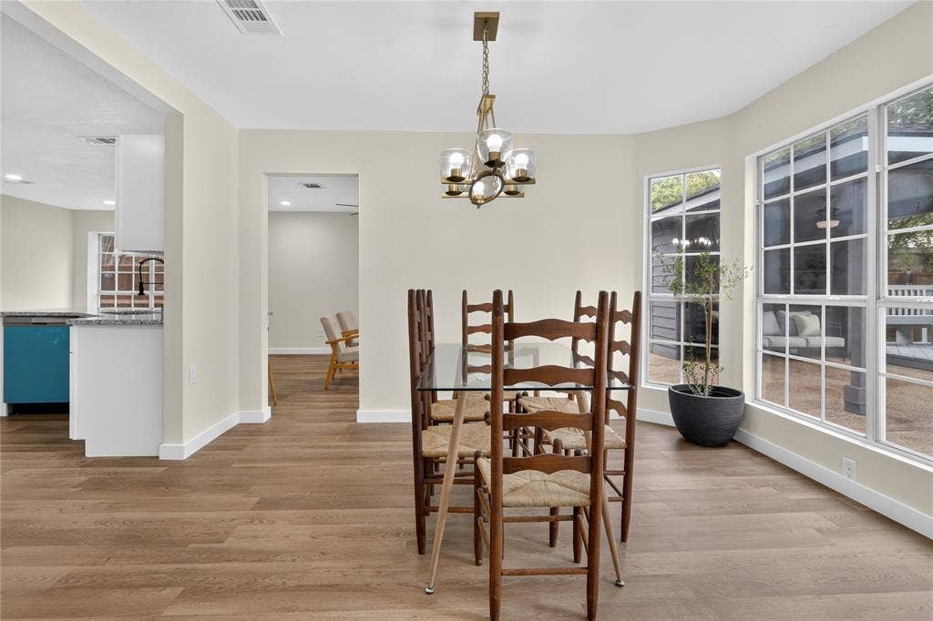 Bright dining area showcasing wood-finish flooring throughout, a brass chandelier, and expansive multi-pane glass doors and windows flooding the space with natural light