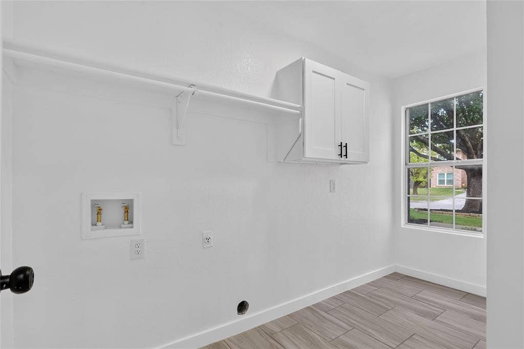 Utility space featuring wood-finish tile flooring, white cabinetry, a built-in wall-mounted hanging rod, and a multi-pane window