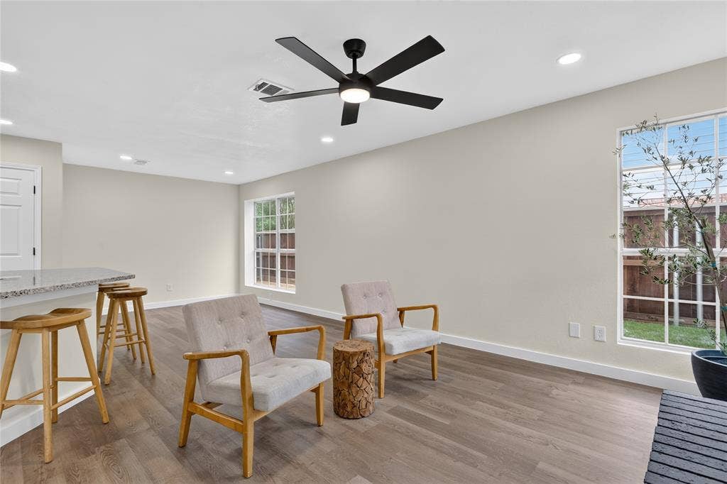 Open-concept interior featuring wood-finish flooring, recessed lighting, a matte black ceiling fan with integrated lighting, a stone-surface breakfast bar, and windows with grid detailing