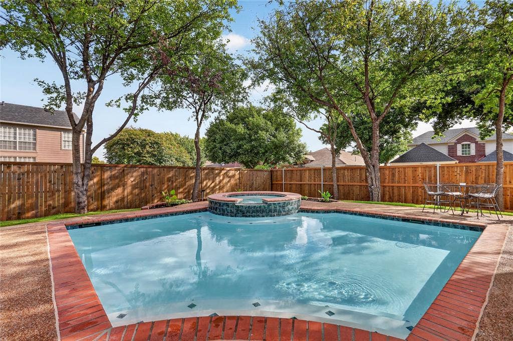 Backyard featuring an in-ground pool, raised spillover spa, brick coping, and a full-height wood privacy fence