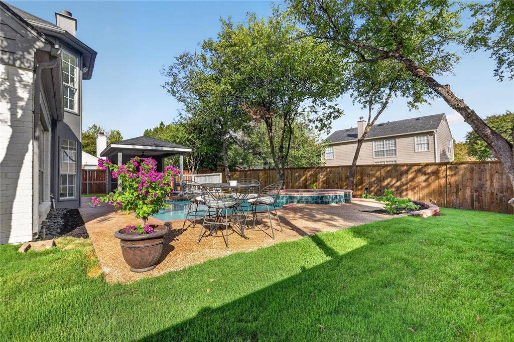 Backyard featuring a covered patio, a pool with a raised spa, decorative stone-finish hardscaping, and perimeter wood fencing