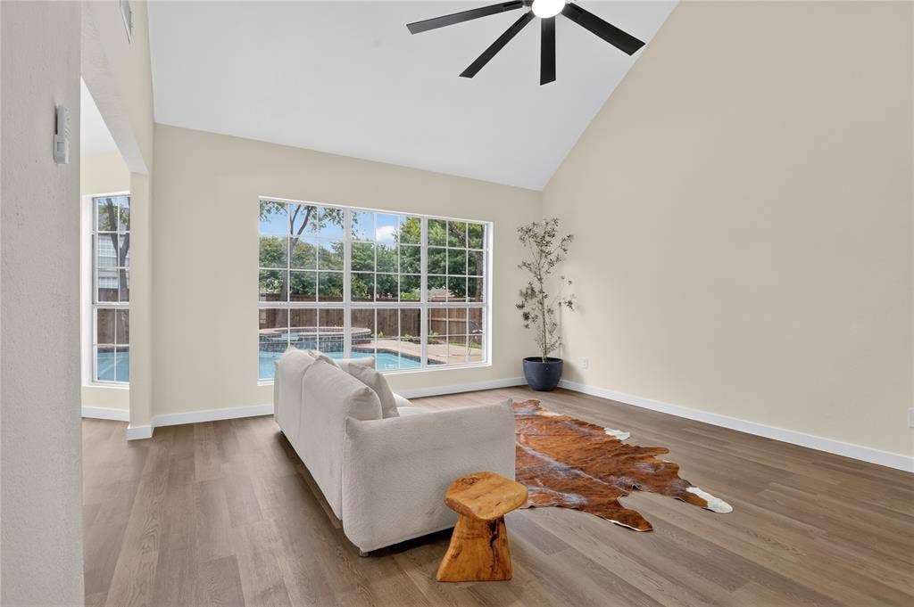Vaulted ceilings with a ceiling fan, wood-finish flooring, and expansive windows featuring outdoor pool access