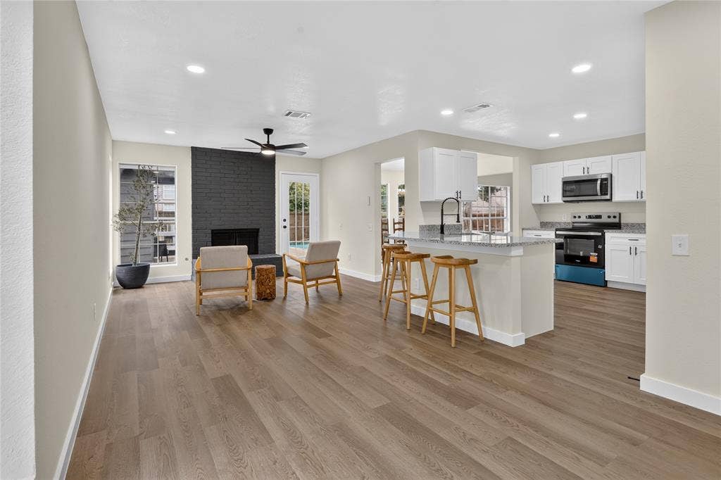 Open-concept interior featuring wood-finish flooring, a floor-to-ceiling brick fireplace, recessed lighting, white kitchen cabinetry, and a kitchen island with a stone-finish countertop