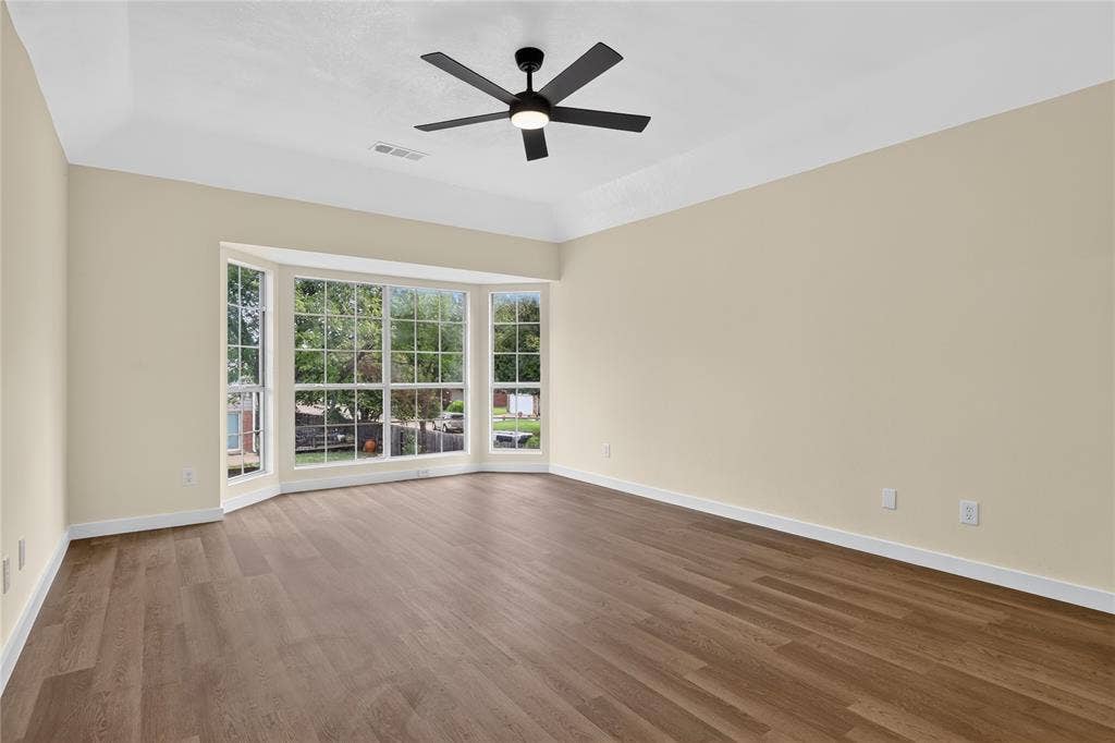 Tray ceiling featuring a contemporary matte black ceiling fan, expansive bay window, and neutral-toned wood-finish flooring