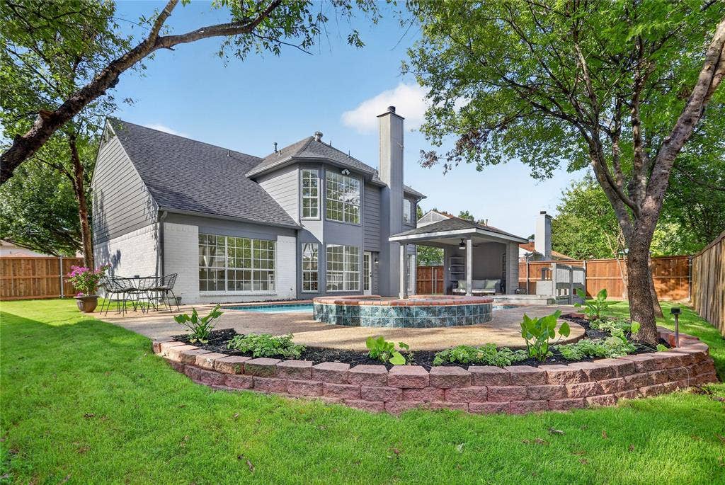 Backyard featuring a swimming pool, raised tile-faced spa, covered patio, stone-texture decking, and terraced stone retaining walls