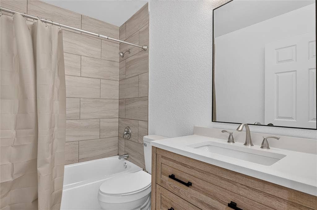 Bathroom featuring a wood-finish vanity with a rectangular sink, a framed mirror, and a tub-shower combination enclosed with horizontal-set tile