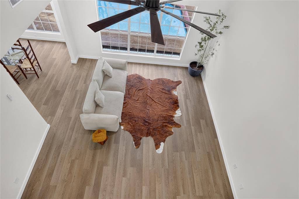 Vaulted ceiling featuring a large dark-finish ceiling fan, wood-finish flooring, and expansive windows