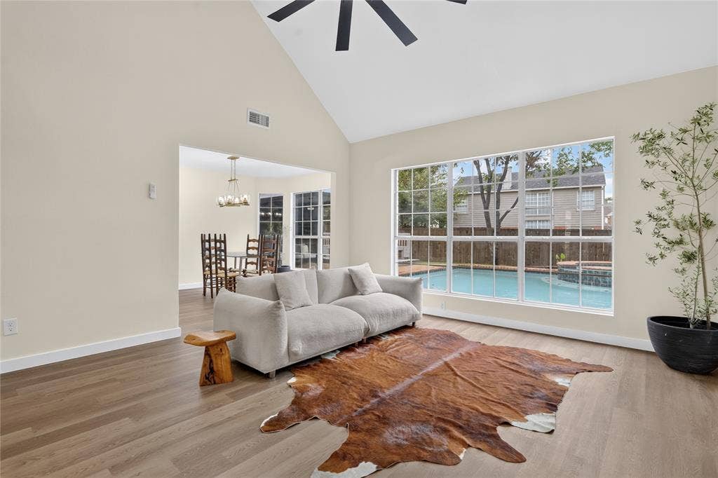 Vaulted ceiling with integrated paddle fan, wood-finish flooring, and expansive windows featuring exterior swimming pool scenery
