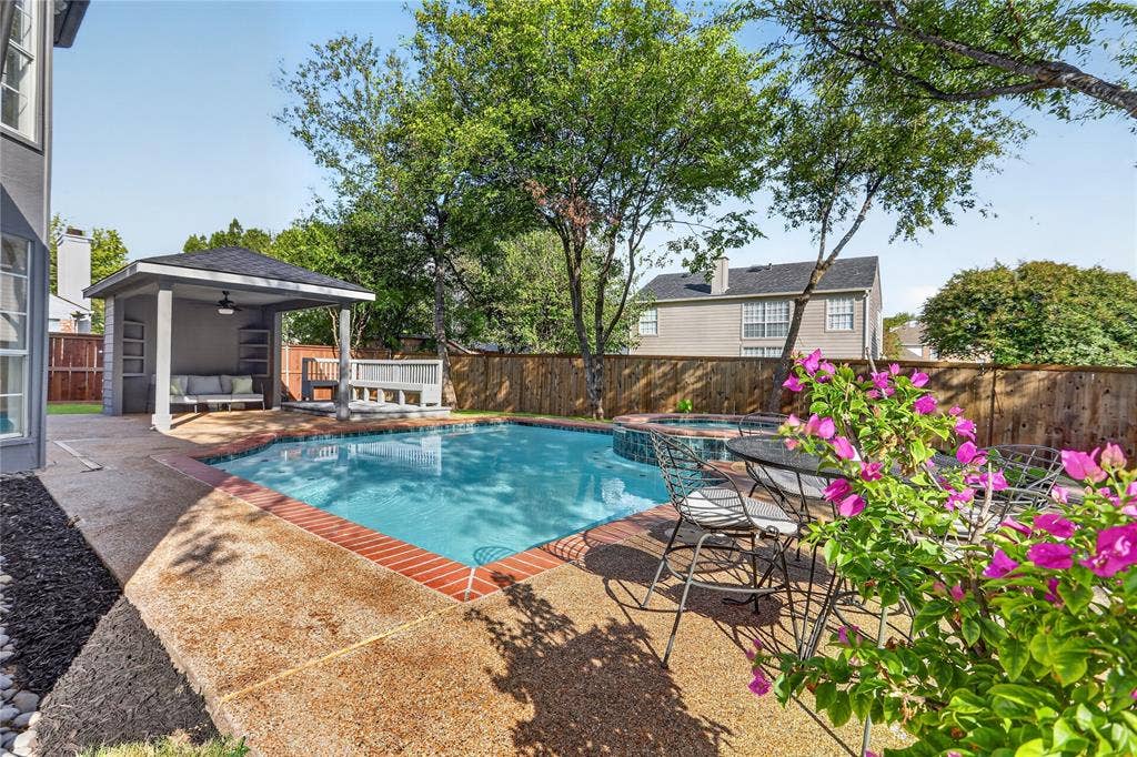 Backyard featuring a swimming pool with brick coping, attached spa, covered pavilion with built-in bench seating, and wood privacy fencing