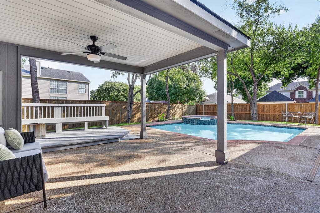 Covered patio with beadboard ceiling and integrated fan, concrete decking, swimming pool with attached spa, and wood privacy fencing