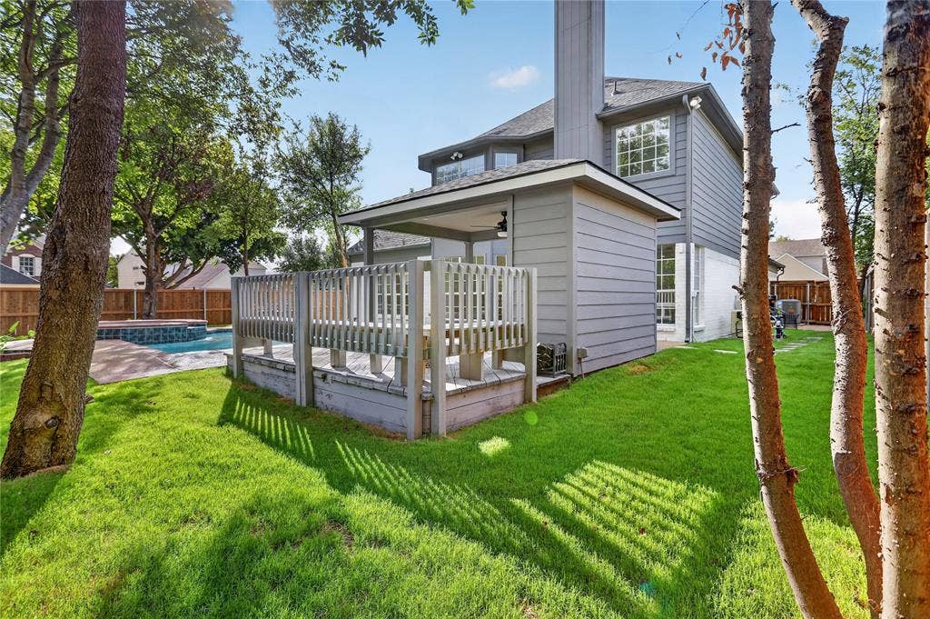 Backyard featuring a raised wooden deck, covered patio, swimming pool with stone coping, and privacy wood fencing