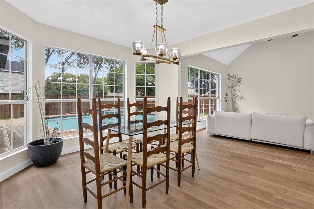 Open-concept area featuring wood-finish flooring, vaulted ceilings, multi-pane windows, and a multi-light metal chandelier