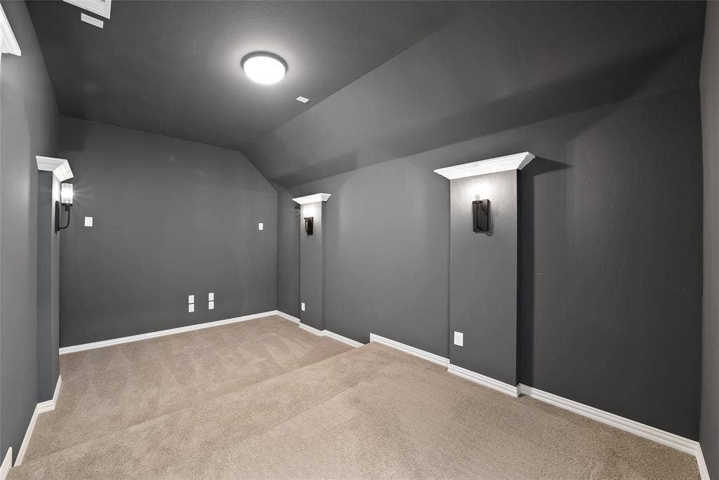 Interior space featuring neutral carpeting, charcoal-toned walls, vaulted ceiling, and recessed wall niches with integrated sconce lighting