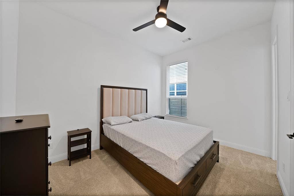 Room featuring neutral wall-to-wall carpeting, a singular window with integrated blinds, and a ceiling-mounted light fixture with a fan