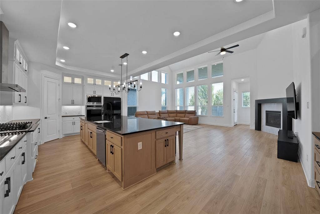 Open-concept living space featuring high ceilings with tray detailing, a central kitchen island with a stone countertop, wood-finish flooring, floor-to-ceiling windows, and a built-in fireplace