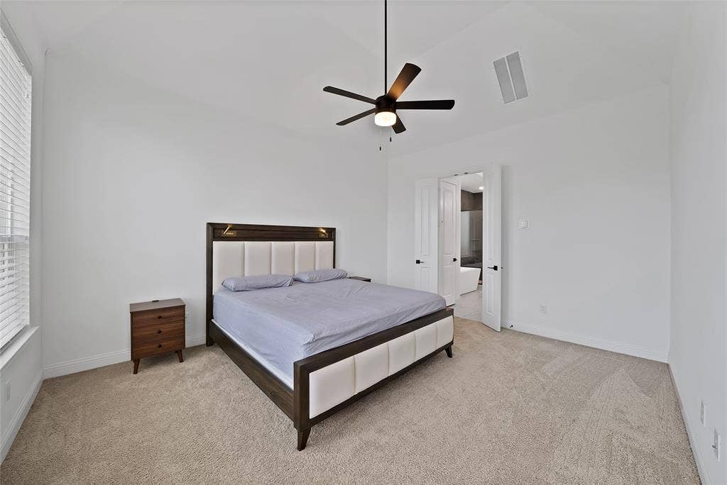 Vaulted ceiling featuring a central matte black ceiling fan with an integrated light fixture, neutral wall-to-wall carpeting, and double-door entry
