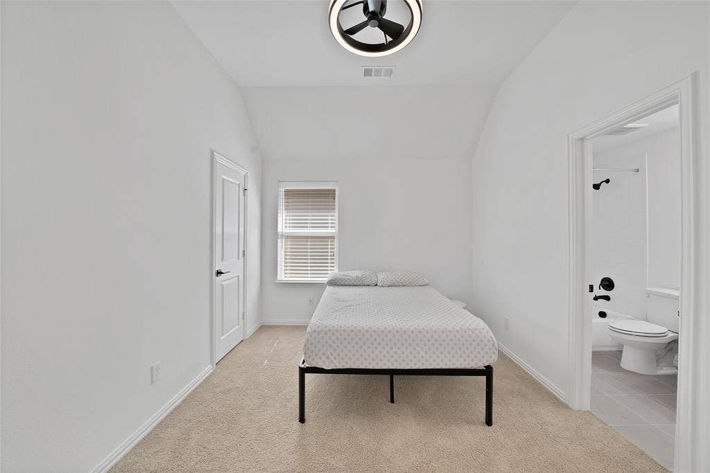 Vaulted ceiling featuring a contemporary circular flush-mount light fixture, neutral wall-to-wall carpeting, and a private bath entry