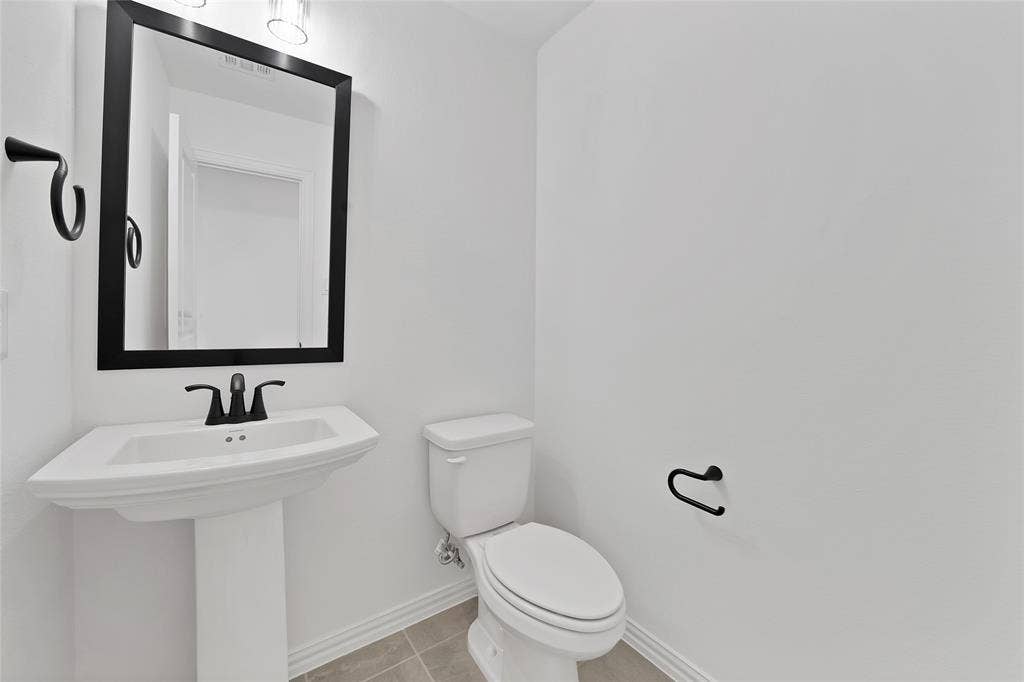 Pedestal sink with a matte black faucet, framed mirror, and tile flooring