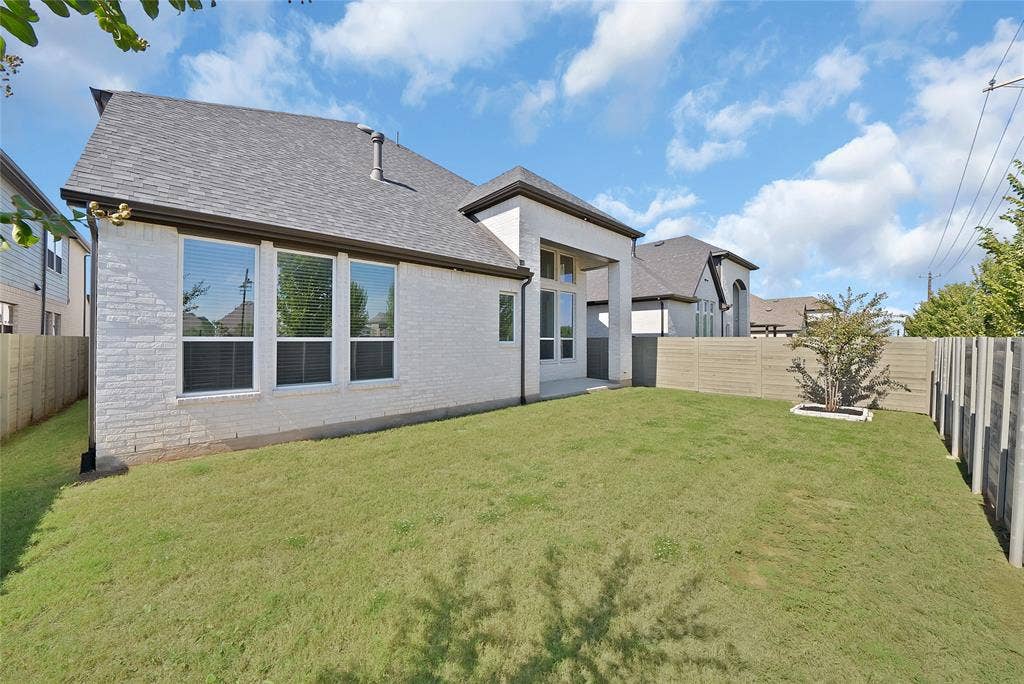 Exterior view featuring painted brick siding, a covered patio, multi-pane windows, asphalt shingle roofing, and a fenced backyard