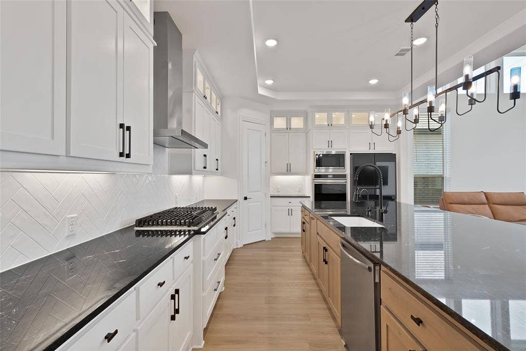 Kitchen featuring white shaker-style cabinetry, dark stone countertops, herringbone-pattern tile backsplash, stainless steel built-in double wall ovens, and a multi-light industrial-style pendant fixture
