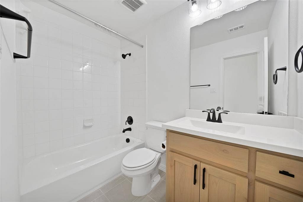 Bathroom featuring a vanity with light wood-finish cabinetry, a solid surface countertop, matte black hardware, and a tile-surround shower and tub combination