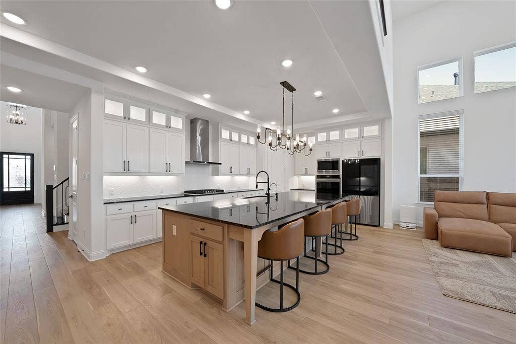 Kitchen featuring shaker-style cabinetry with glass-front uppers, a central island with wood-finish base, dark stone countertops, recessed lighting, and high ceilings